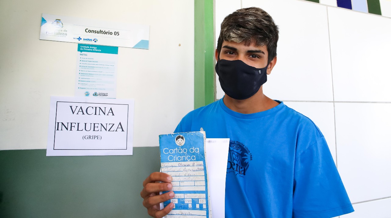 adolescente com máscara mostra a capa da sua caderneta de vacinação